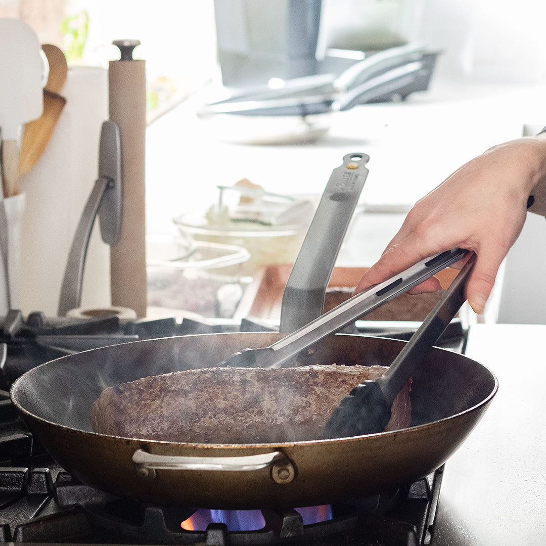 A person holding a tenderloin with tongs and searing it on all sides in a skillet pan.